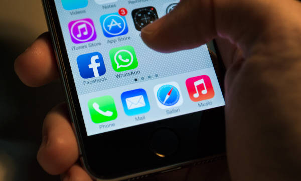 O mână care ține un telefon, cu câteva aplicații afișate pe ecranul telefonului