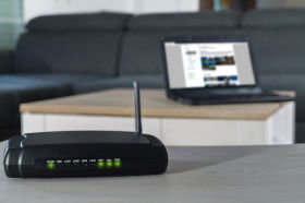 Router Wi-Fi în fața unei canapele și a unui laptop