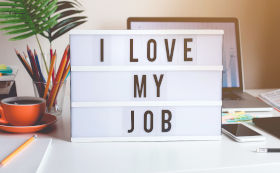 A card on a table saying I love my job with a computer in the background